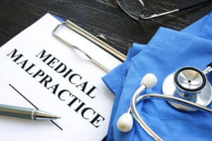 Scrubs, a stethoscope, and a clipboard on a table. The clipboard has a piece of paper that says “Medical Malpractice”